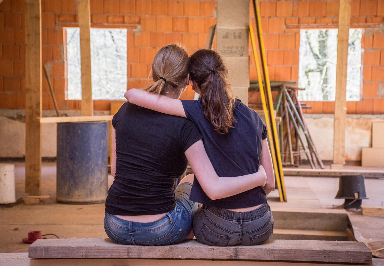 Zwei Frauen sitzen Arm in Arm im Rohbau ihres Hauses
